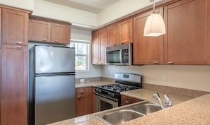 A kitchen with wooden cabinets, stainless steel appliances, granite countertops, and a pendant light. - 1 Bedroom In Central Marina Del Rey - Close To Beach (Marina del Rey)