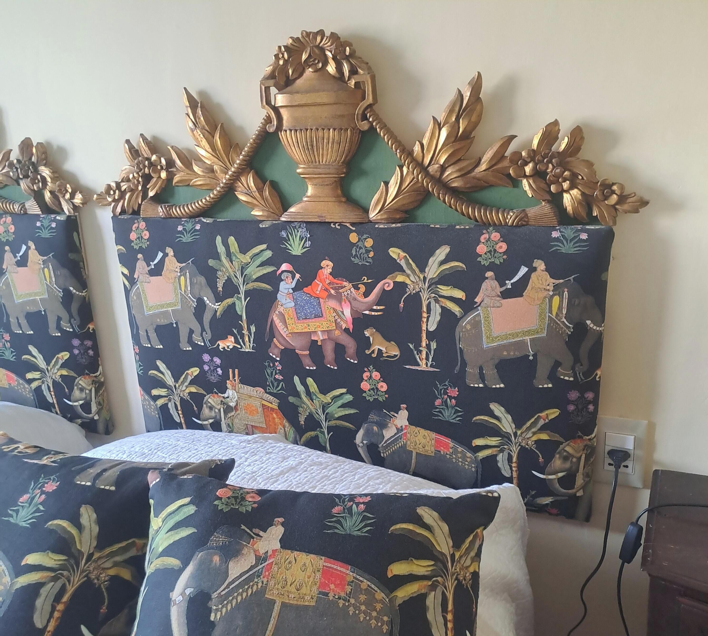 Una stanza con una testiera decorata, caratterizzata da una grande urna e motivi fogliacei elaborati. La testiera presenta un tessuto scuro con disegni di elefanti e fiori.
