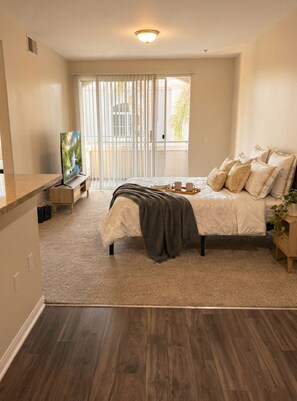 A bedroom with a bed, a TV, a bedside table, and a window with blinds. - Cozy 1-bedroom apartment in delightful Marina del Rey with AC (Marina del Rey)