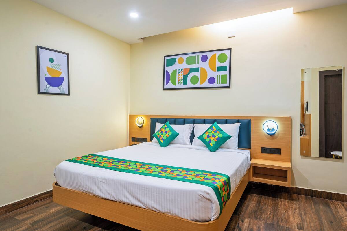 Un lit bien fait, recouvert d’une couvre-lit à motifs, une tête de lit dotée d’un éclairage intégré et deux œuvres d’art accrochées au mur.