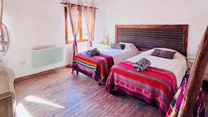 A room with two beds, wooden beams on the ceiling, a radiator, and a window with curtains. - La Nochera Killa Cabins (Tilcara)