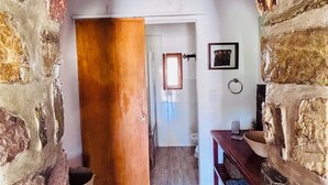 A narrow stone corridor leading to a room with a wooden door, a white wall with a framed picture, and a wooden bench with a bowl. - La Nochera Killa Cabins (Tilcara)