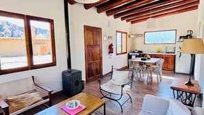 A cozy living room with a wooden ceiling, a sofa, a coffee table, and a dining area with a table and chairs. - La Nochera Killa Cabins (Tilcara)
