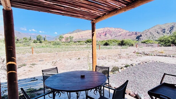 An outdoor patio with a wooden pergola, a round table, and four chairs. - La Nochera Killa Cabins (Tilcara)
