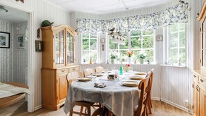 Een eetkamer met een houten tafel gedekt voor zes personen, omringd door stoelen. Links bevindt zich een houten kast met glazen deuren.