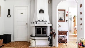 Een gezellige woonkamer met een witte schoorsteen, houten vloer, een deur met een klein bordje, en een rieten mand met kleurrijke spullen.