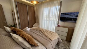 Un dormitorio con cama, mesita de noche, televisor y ventana con cortinas.