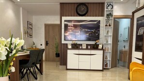 Una sala moderna con un televisor de pantalla plana, un comedor con mesa y sillas, y un rincón de descanso acogedor con un sofá verde.