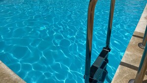Una piscina con agua azul cristalina y una escalera metálica.