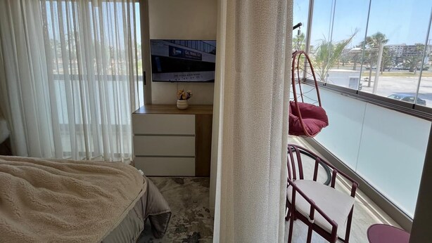 Habitación de hotel con cama, escritorio con televisor de pantalla plana, silla y ventana grande con vista a un estacionamiento y edificios.