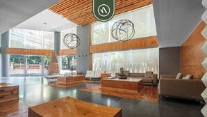 Un vestíbulo amplio con suelo de madera, una zona de estar central con sofá y mesa de centro, y ventanas grandes que permiten la entrada de luz natural.