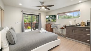 A modern bedroom with a bed, a ceiling fan, a TV, a desk, and a window with a view of greenery. - NEW Cimaron Butte Studio Laundry Kitchenette (Sedona)