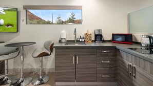 A modern kitchen with a large window, a flat-screen TV, a coffee maker, and a microwave. - NEW Cimaron Butte Studio Laundry Kitchenette (Sedona)