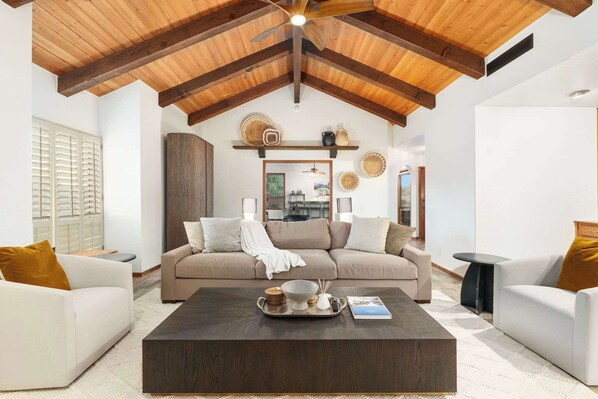 A living room with a high ceiling, wooden beams, a beige sofa, white armchairs, and a coffee table with decorative items. - NEW 2M Luxe N Scottsdale Estate w Heated Pool (Scottsdale)
