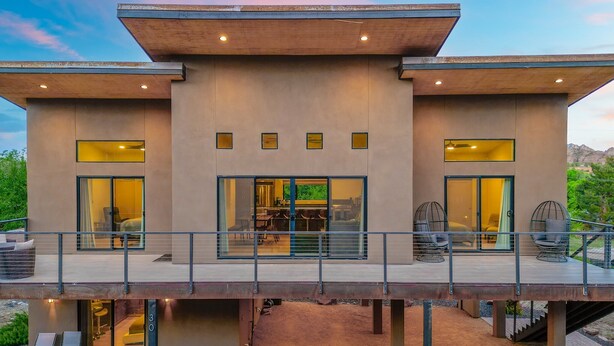 A modern two-story house with a covered outdoor deck, large sliding glass doors, and a visible interior with a dining area and seating. - NEW Cimaron Butte View Terrace 2 Kings Firepit (Sedona)