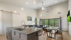 A modern kitchen with a central island, a dining area with a table and chairs, and a large window providing a view of trees. - NEW Cimaron Butte View Terrace 2 Kings Firepit (Sedona)