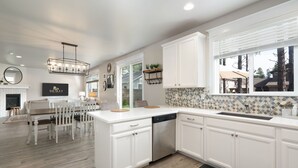 A modern kitchen with white cabinetry, a central island, and a dining area with a wooden table and chairs. - NEW Alamo Alpine Retreat Sleeps 11 3 Showers (Flagstaff)