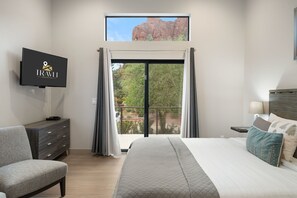 Una habitación de hotel con cama, televisor montado en la pared, escritorio y vista a un paisaje rocoso a través de un ventanal grande.