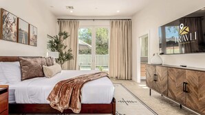 Une chambre à coucher avec un lit, une télévision, une armoire en bois et un balcon avec des rideaux.