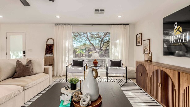 Un salon moderne avec un canapé, une table basse agrémentée d’objets décoratifs, une vue sur l’extérieur grâce à de grandes fenêtres et un panneau mural.