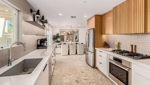 Une cuisine moderne avec des meubles blancs, un réfrigérateur en acier inoxydable et une cuisinière à gaz.