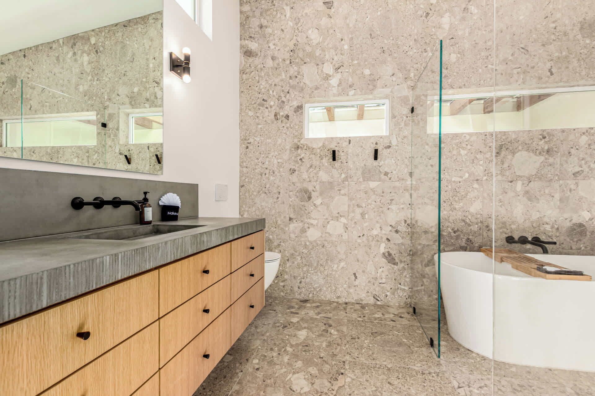 Une salle de bain moderne avec un comptoir en granit, des meubles en bois, un grand miroir et une baignoire sur pieds.