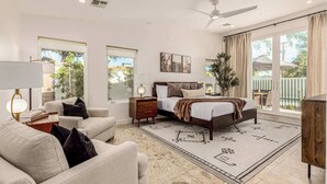 Une chambre spacieuse avec un grand lit, un coin salon avec un canapé et un fauteuil, un coin repas avec une table et des chaises, et un balcon avec vue.