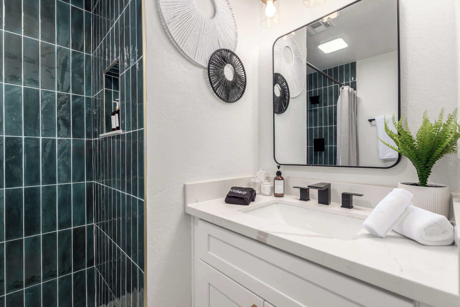 Une salle de bain moderne avec un meuble-lavabo blanc, un grand miroir et une zone de douche carrelée de carreaux verts.