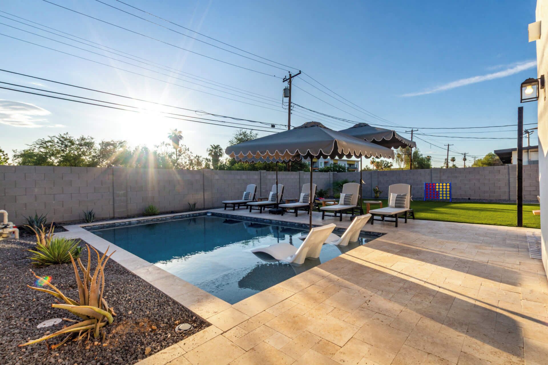 A swimming pool with lounge chairs and umbrellas, surrounded by a brick wall and a grassy area.