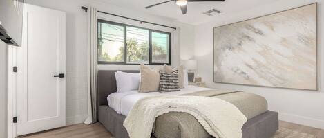 A bedroom with a bed, a ceiling fan, a window, and a large abstract painting on the wall.