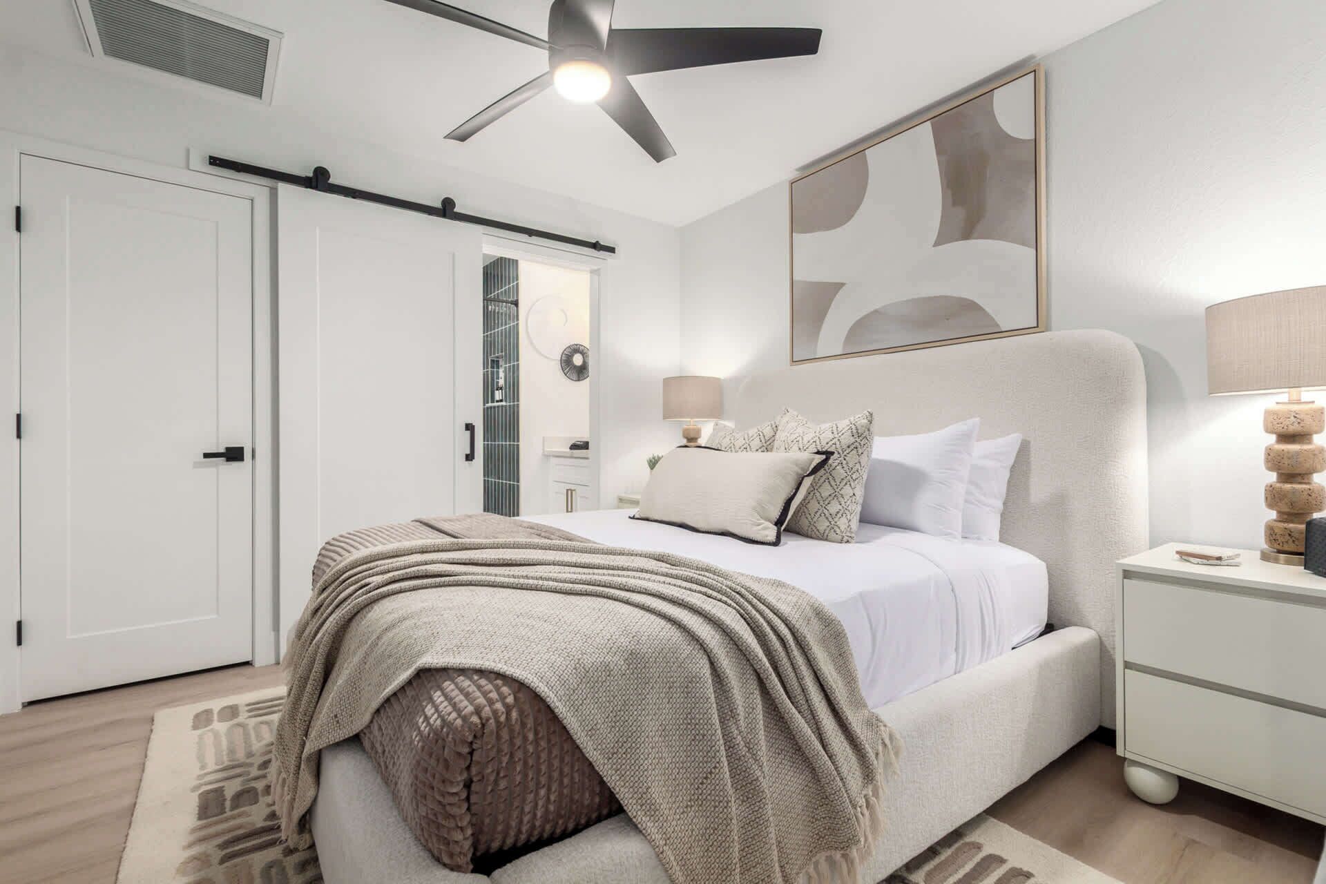 A bedroom with a bed, bedside tables, a ceiling fan, and a large abstract painting on the wall.