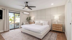 Ein modernes Schlafzimmer mit einem großen Bett, zwei Nachttischen, einem Deckenventilator und einer Glastür, die zu einem Außenbereich führt.