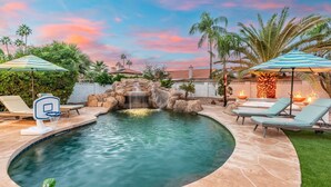 A swimming pool with a waterfall feature, lounge chairs, and umbrellas. - NEW Grotto Falls Retreat Pool w Slide Spa Putt Grn (Scottsdale)