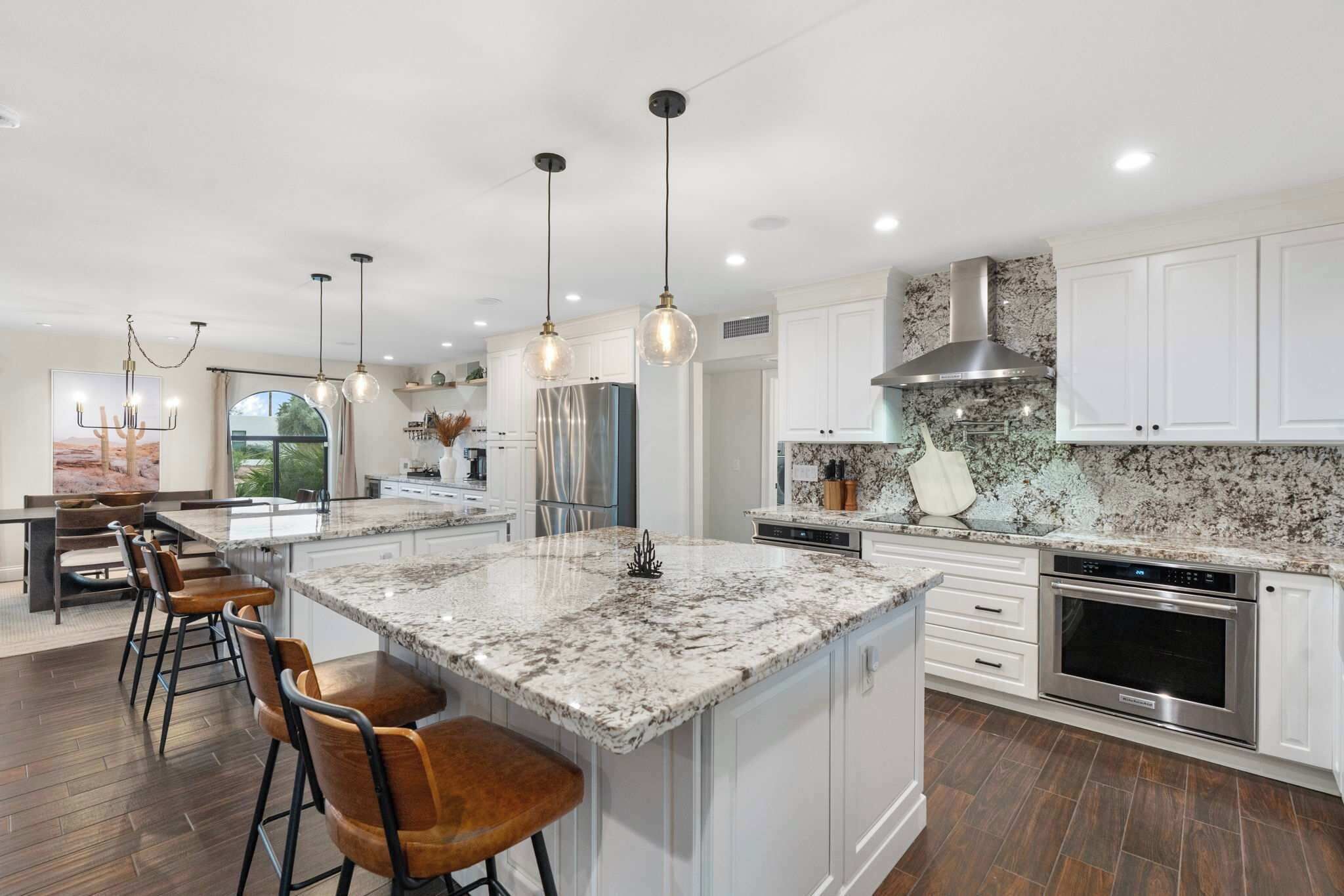 A modern kitchen with white cabinets, a large island with bar stools, stainless steel appliances, and pendant lighting.