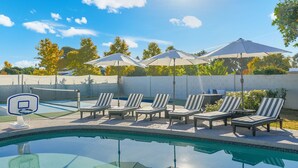 A swimming pool with lounge chairs and umbrellas, surrounded by a brick wall and trees. - NEW Casa Bravada Heated Pool Spa Pickleball (Scottsdale)
