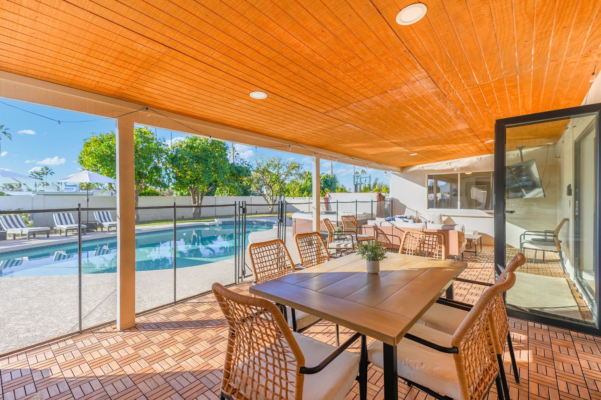 An outdoor patio with a wooden ceiling, a pool, wicker furniture, and a view of the pool area.