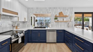 A modern kitchen with white cabinets, blue accents, and a view to the outdoor seating area. - NEW Casa Bravada Heated Pool Spa Pickleball (Scottsdale)