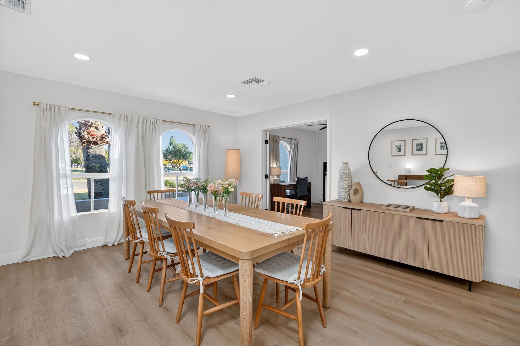 A modern dining room with a wooden table and chairs, a kitchen area with a wooden counter, and a large mirror on the wall.