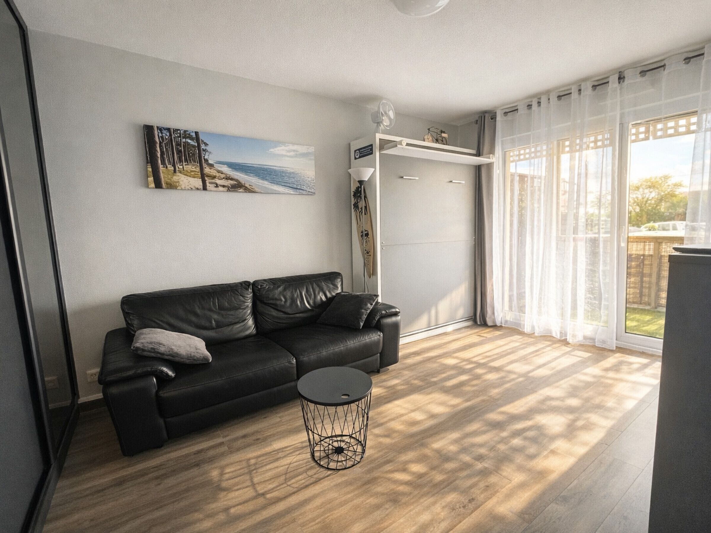 Un salon moderne avec un canapé en cuir noir, une table basse ronde et un tableau représentant une scène de plage.