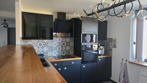 A modern kitchen with black cabinets, a wooden countertop, a built-in microwave, and a hanging light fixture.