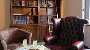 A library with bookshelves, a leather armchair, and two glasses of drink on a table.