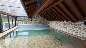 An indoor swimming pool with stone walls and a wooden ceiling.