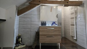 A modern bathroom with a wooden ceiling, a large mirror, a sink with toiletries, and a statue.