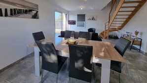Un comedor moderno con una mesa de madera y sillas negras, una escalera y vistas al exterior.