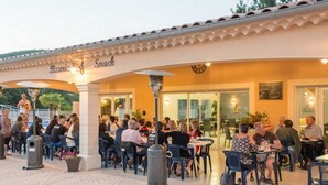 An outdoor seating area with tables and chairs, a covered walkway, and a building with a sign reading "Pizza & Snack". - Mobile home for 6 ppl with terrace (Saint-Maurice-d'Ibie)