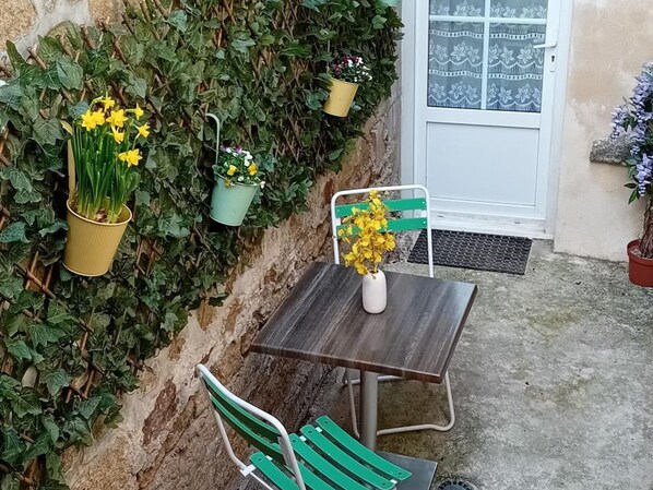 A small outdoor seating area with a table and two chairs, surrounded by a wall covered in green foliage and potted plants. - Charming house in the center of Carrouges with WIFI (Carrouges)