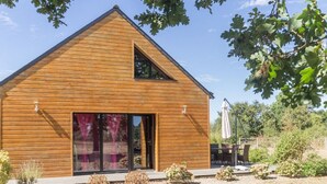 Ein modernes Holzhaus mit einer großen Schiebeglastür, einem kleinen Dachfenster und einem Schotterweg.