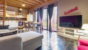 Ein modernes Wohnzimmer mit Sofa, Fernseher und einer Küche im Hintergrund.
