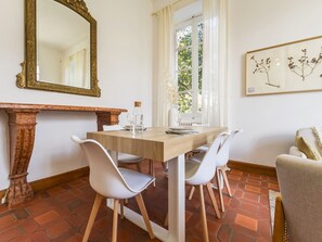 Un comedor con mesa de madera, sillas blancas, un espejo grande y un ventanal con cortinas.
