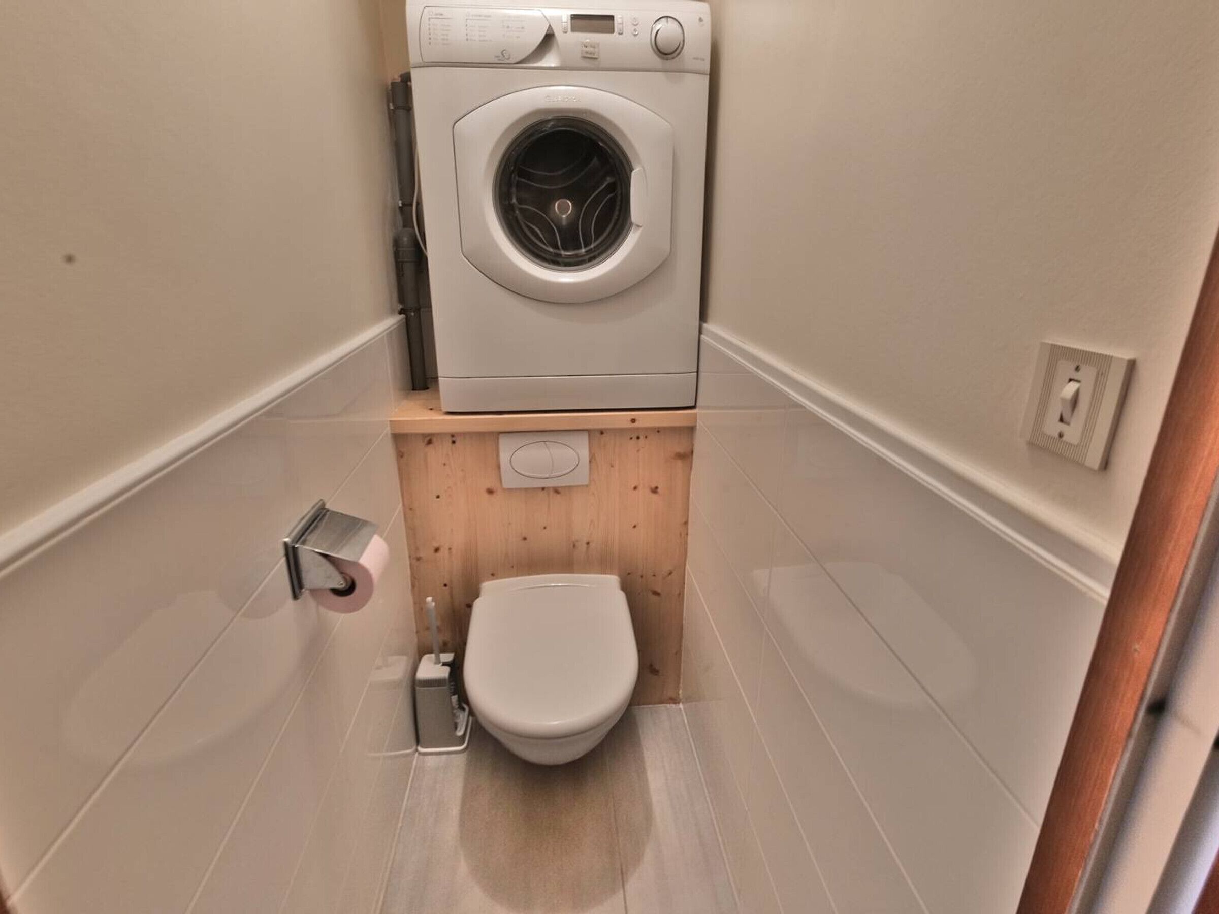Ein kleines Badezimmer mit Toilette, einem Holzboden und einer Waschmaschine.